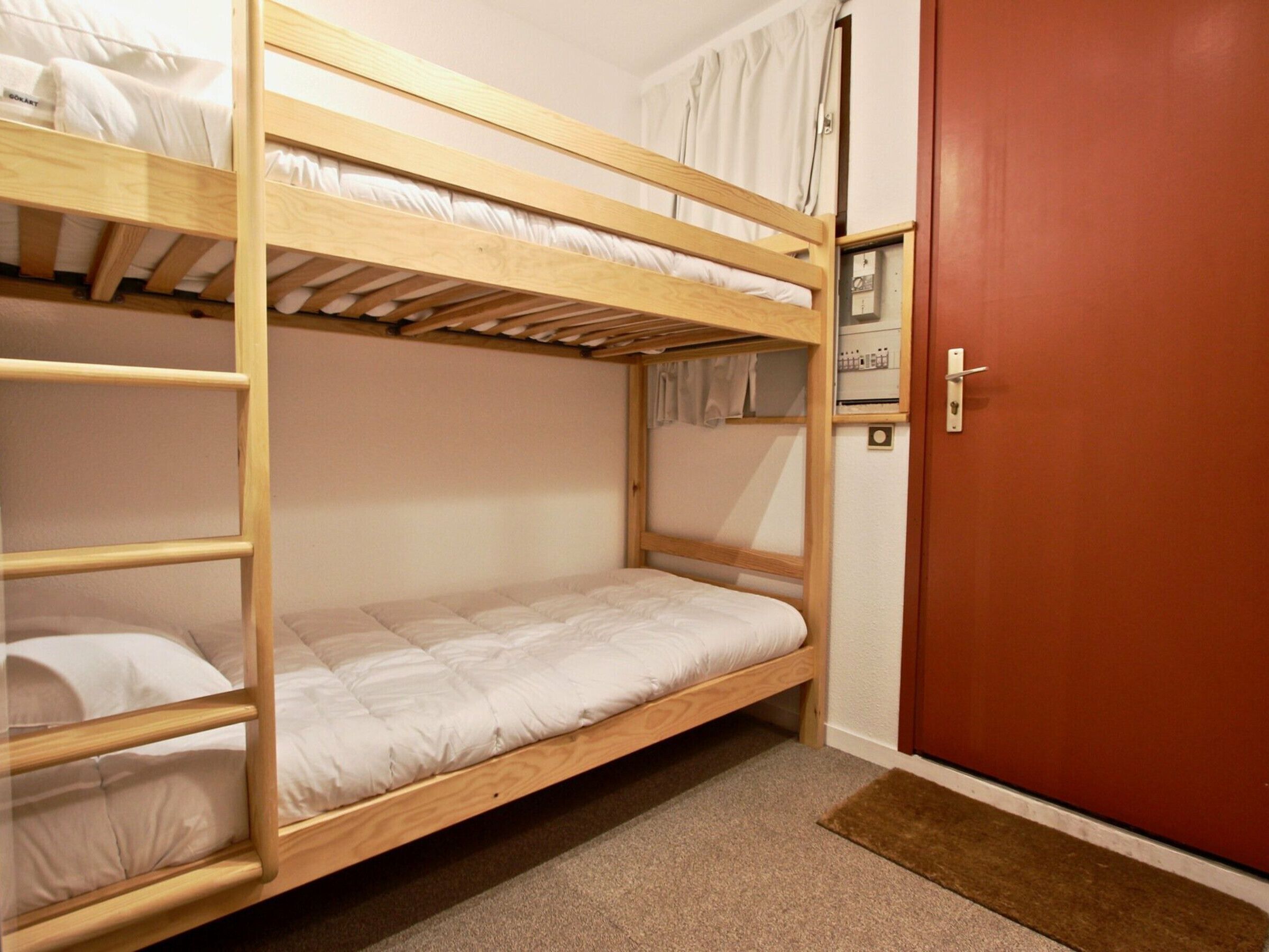 A bunk bed room with a wooden frame, a door, and a carpeted floor.