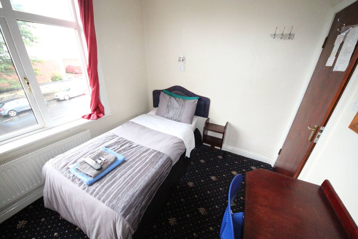 A small, neatly arranged bedroom with a bed, a chair, and a window with a view of the street outside.