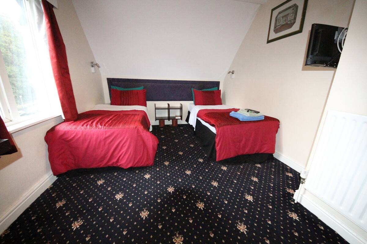 A room with two single beds, a small table, and a window with red curtains.