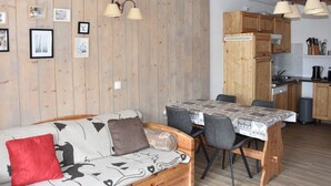 Un salon chaleureux avec un canapé, une table à manger et des chaises, des murs en bois et un coin cuisine doté de meubles en bois et d’une cuisinière.