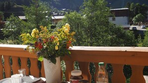 Un balcon avec une table dressée pour deux personnes, un vase de fleurs et des pots de Nutella et de jus d’orange.