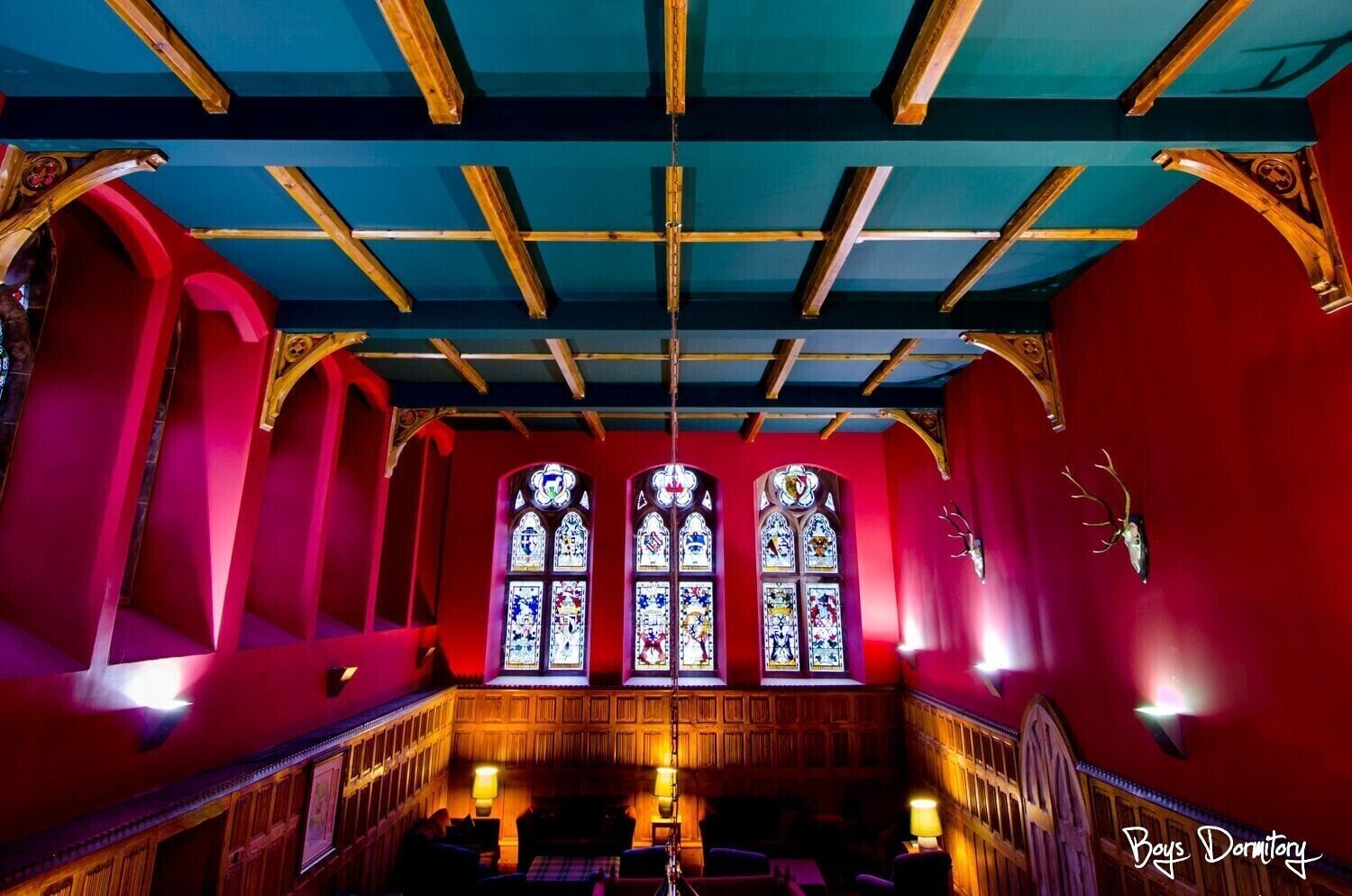 A church interior with red walls, wooden pews, stained glass windows, and a high ceiling with wooden beams.
