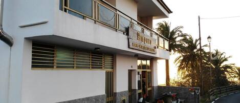 A two-story building with a sign reading "Amparo Bar Restaurant" on the ground floor. There is a small outdoor seating area with a table and chairs.