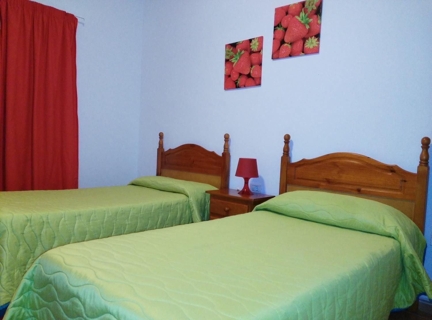 Habitació amb dos llits individuals, un capçal de llit de fusta, una tauleta de nit amb una làmpada vermella i dues obres d'art murals de fresons.