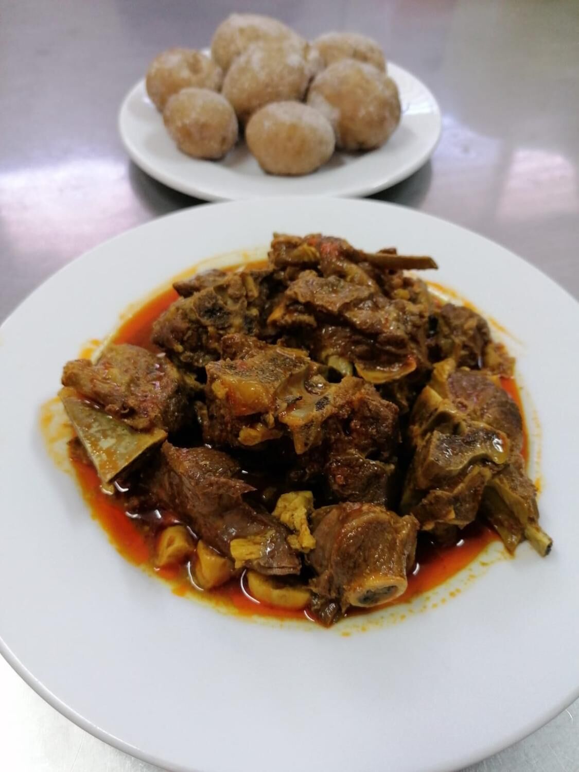 A plate of meat stew with bones and a side of round, golden-brown bread.