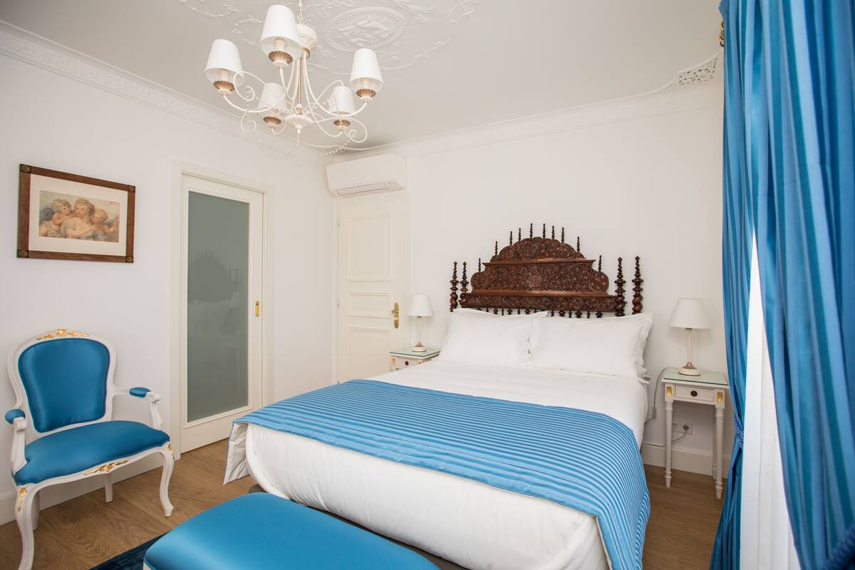 A bedroom with a large bed, a chair, a nightstand, and a chandelier.