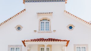 A building with a white facade, a tiled roof, and multiple windows with white frames.