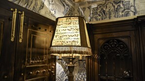 A room with a large ornate lamp, dark wooden doors, and a marble wall with intricate designs.