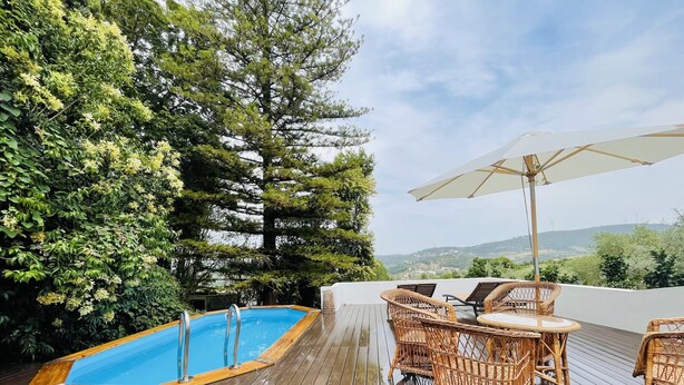 A wooden deck with a swimming pool, wicker furniture, and a view of the landscape.