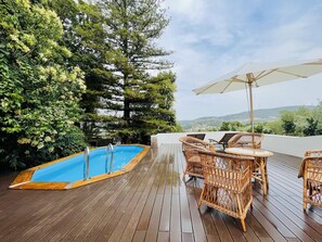A wooden deck with a swimming pool, wicker furniture, and a view of the landscape. - Sra da Oliveira Solar Heritage (Leiria)