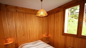 A wooden room with a bed, a window, and a hanging light fixture. - Lovely 2-room cabin 7 pers, slope view (Hauteluce)