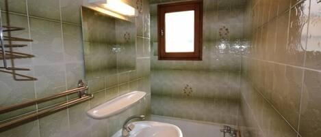 A bathroom with a sink, bathtub, and a window.