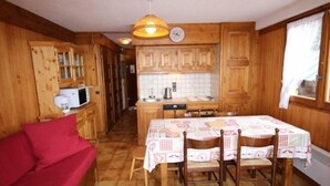 A wooden interior with a dining table, chairs, a red sofa, wooden cabinets, a microwave, and a clock. - Lovely 2-room cabin 7 pers, slope view (Hauteluce)