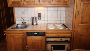 A kitchen with wooden cabinets, a stainless steel sink, a kettle, a stove, and a dishwasher. - Lovely 2-room cabin 7 pers, slope view (Hauteluce)