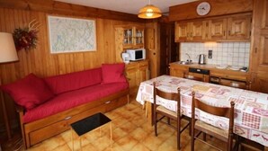 A cozy cabin interior with a red sofa, wooden dining table, and a kitchen area with wooden cabinets and a microwave. - Lovely 2-room cabin 7 pers, slope view (Hauteluce)