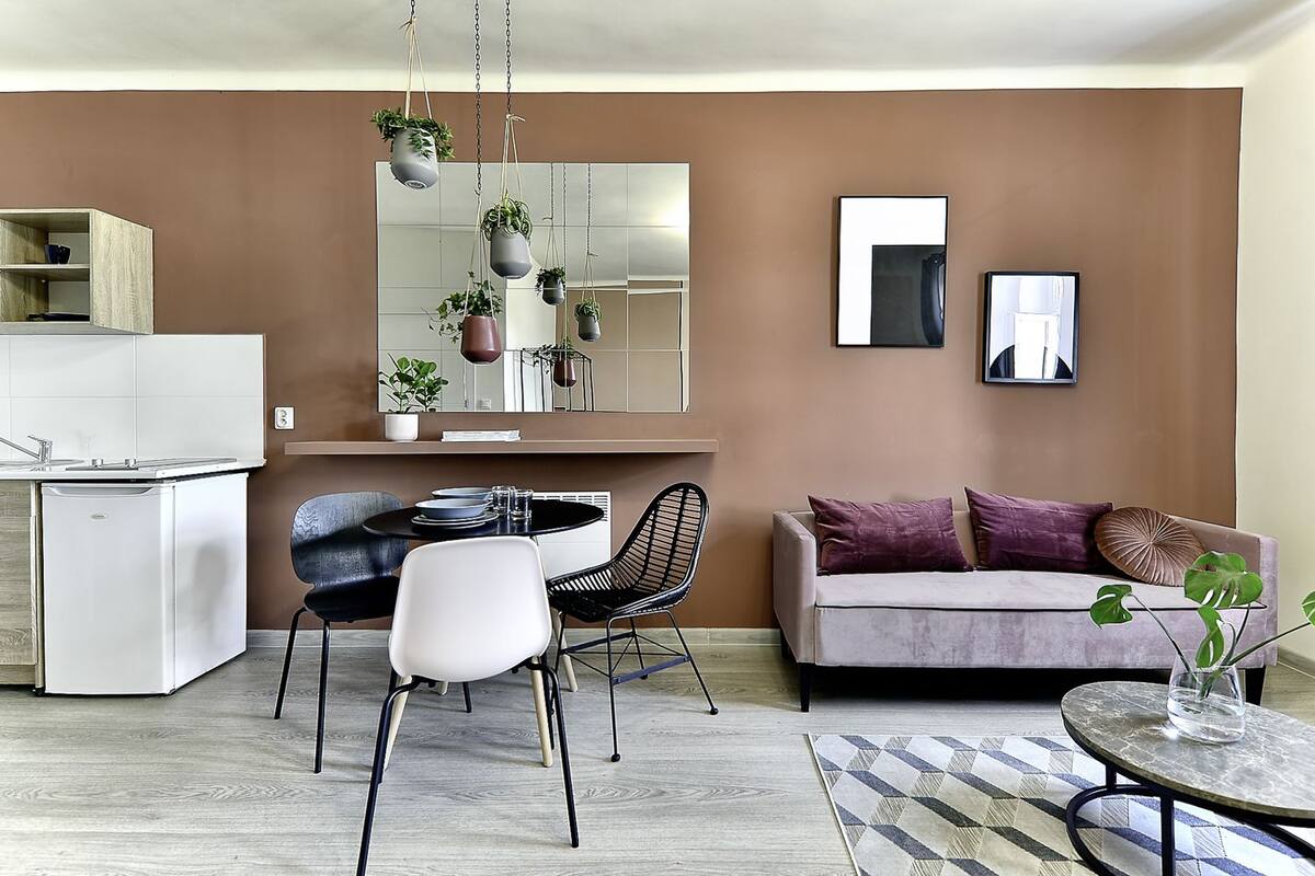 A modern living room with a sofa, dining table, chairs, and a kitchen area.