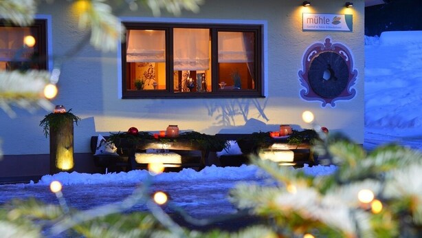 A hotel exterior with a clock, a sign, and outdoor seating with lights. - Gasthof Mühle Natur- & Wanderhotel (Rinchnach)