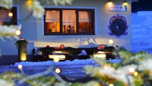 Exterior de un hotel con un reloj, un cartel y mesas exteriores con iluminación.