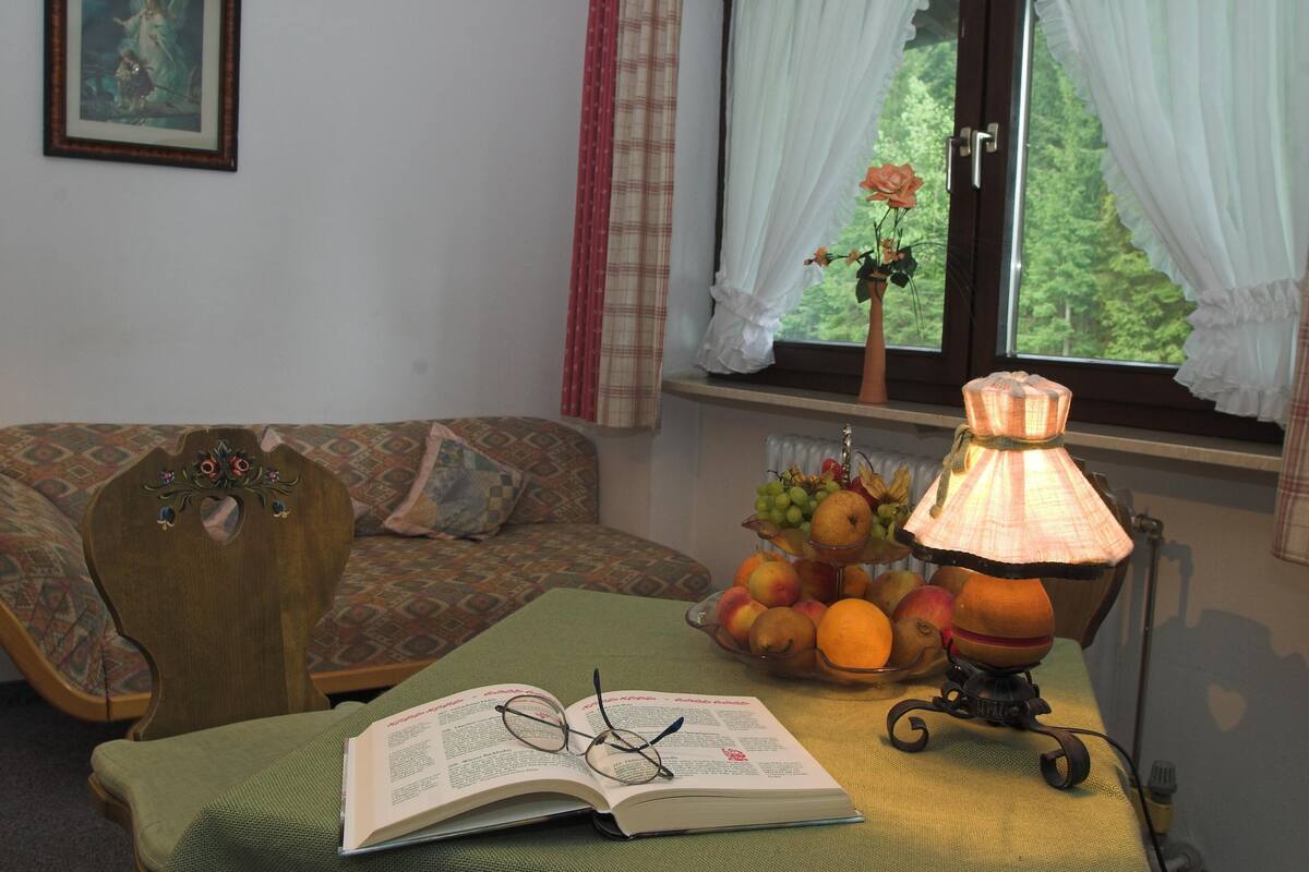 A cozy room with a patterned sofa, a table with a lamp, a bowl of fruit, and an open book.