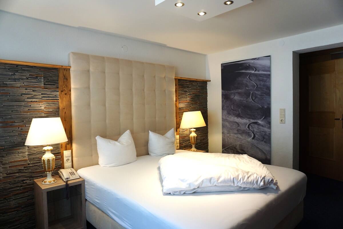 Ein Hotelzimmer mit einem großen Bett, zwei Nachttischlampen, einem Telefon auf dem Nachttisch und einer Steinwand.