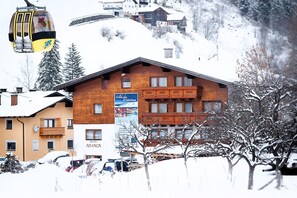 A hotel with a wooden facade, a signboard, and a ski lift in the background. - Hotel ad LACA (See)