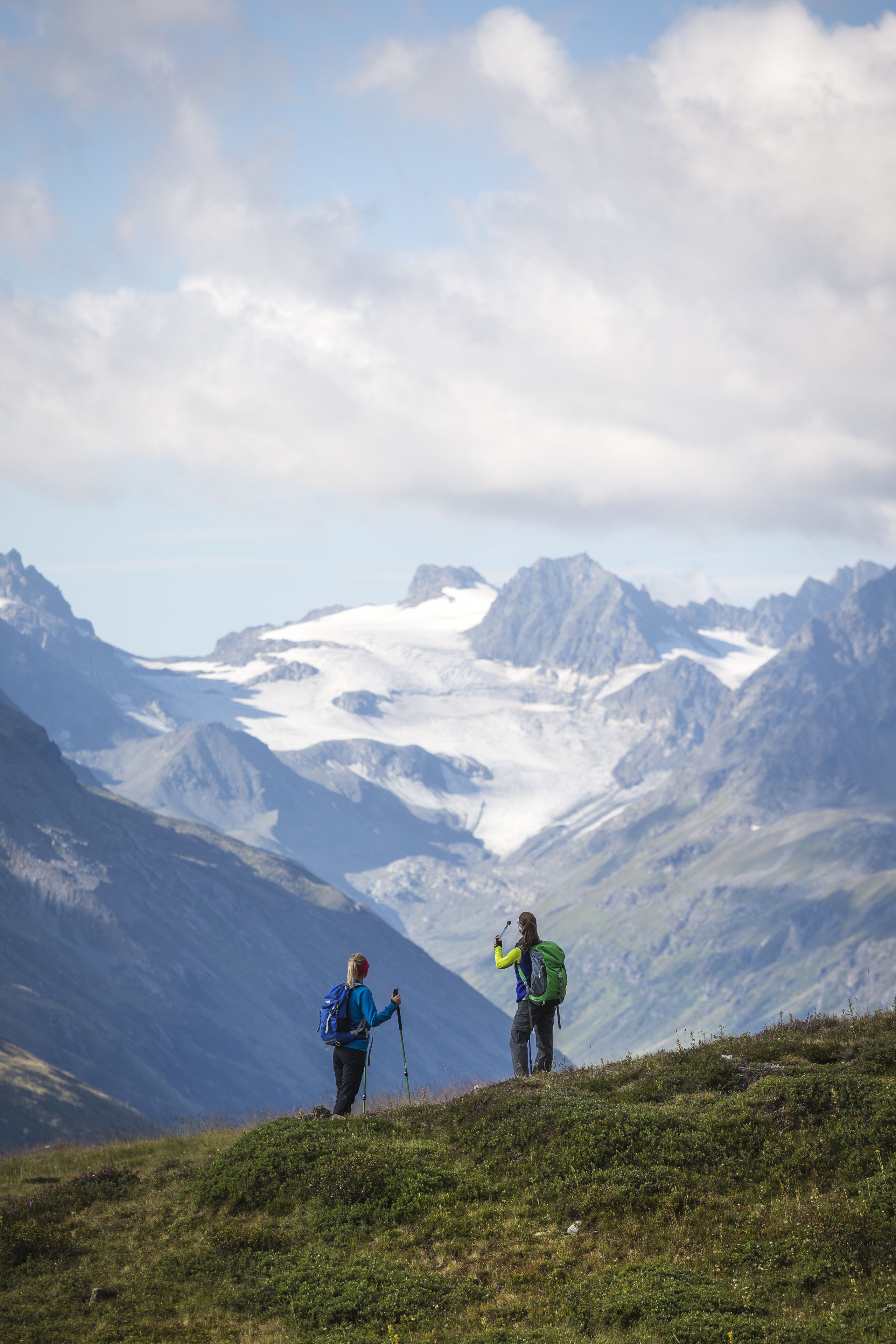 Dos excursionistas en un sendero de montaña con un glaciar al fondo.