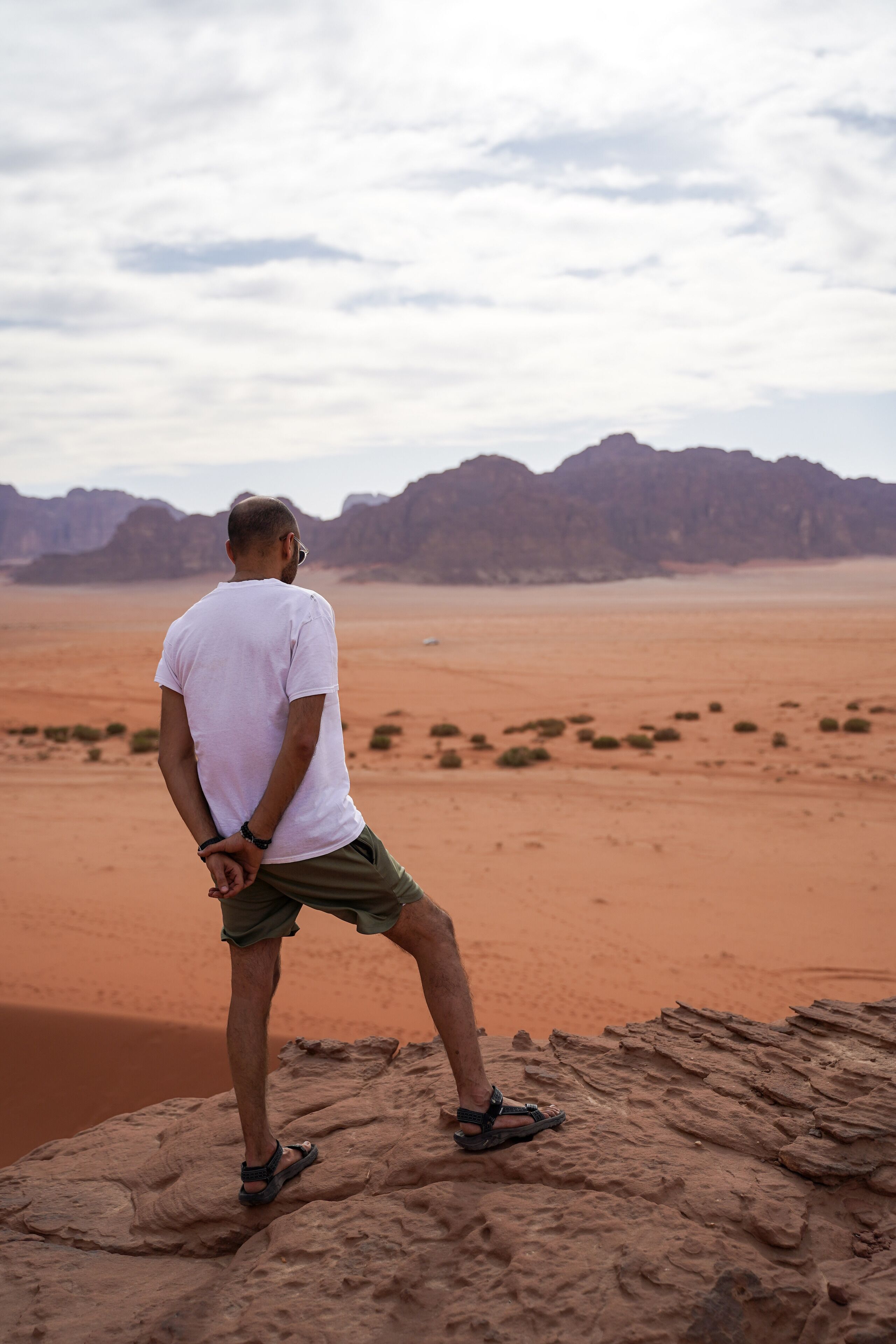 A person standing on a rock in a desert landscape with mountains in the background.