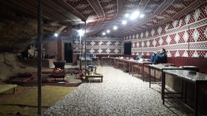 A traditional room with patterned walls, a central fire pit, and a long table with benches. - Bedouin Sunrise camp (Wadi Rum)