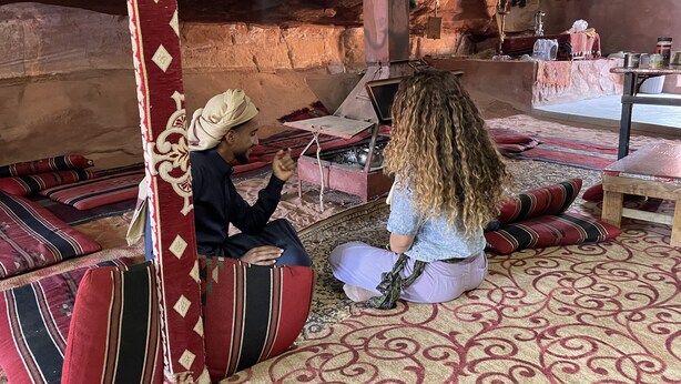 A traditional setting with a stone wall, a wooden table, and a patterned carpet. - Bedouin Sunrise camp (Wadi Rum)