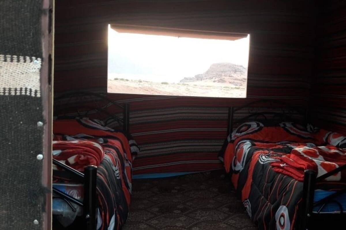 Une chambre avec deux lits, une fenêtre donnant sur un paysage désertique et un mur décoré de motifs.