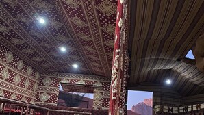 An interior with patterned carpets, a large window, and a vehicle outside. - Bedouin Sunrise camp (Wadi Rum)