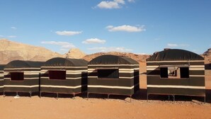 Four dome-shaped tents with striped patterns, arranged in a row on a dirt ground with a desert landscape in the background. - Bedouin Sunrise camp (Wadi Rum)