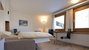 Ein Hotelzimmer mit Bett, Schreibtisch, Stuhl, Lampe und einem Fenster mit Vorhängen.