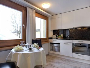 Une cuisine moderne avec des meubles blancs, un plan de travail noir et un coin repas avec une table mise pour deux personnes.