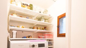 A compact laundry room with a front-loading Whirlpool washer, shelves above for storage, and a small window. - Your home in Trequanda (Trequanda)