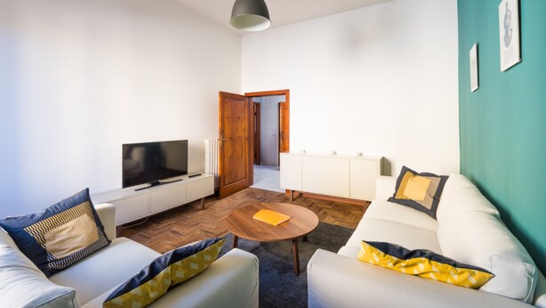 A modern living room with a sofa, armchair, and a coffee table. A television is mounted on the wall, and there is a wooden door leading to another room. - Your home in Trequanda (Trequanda)