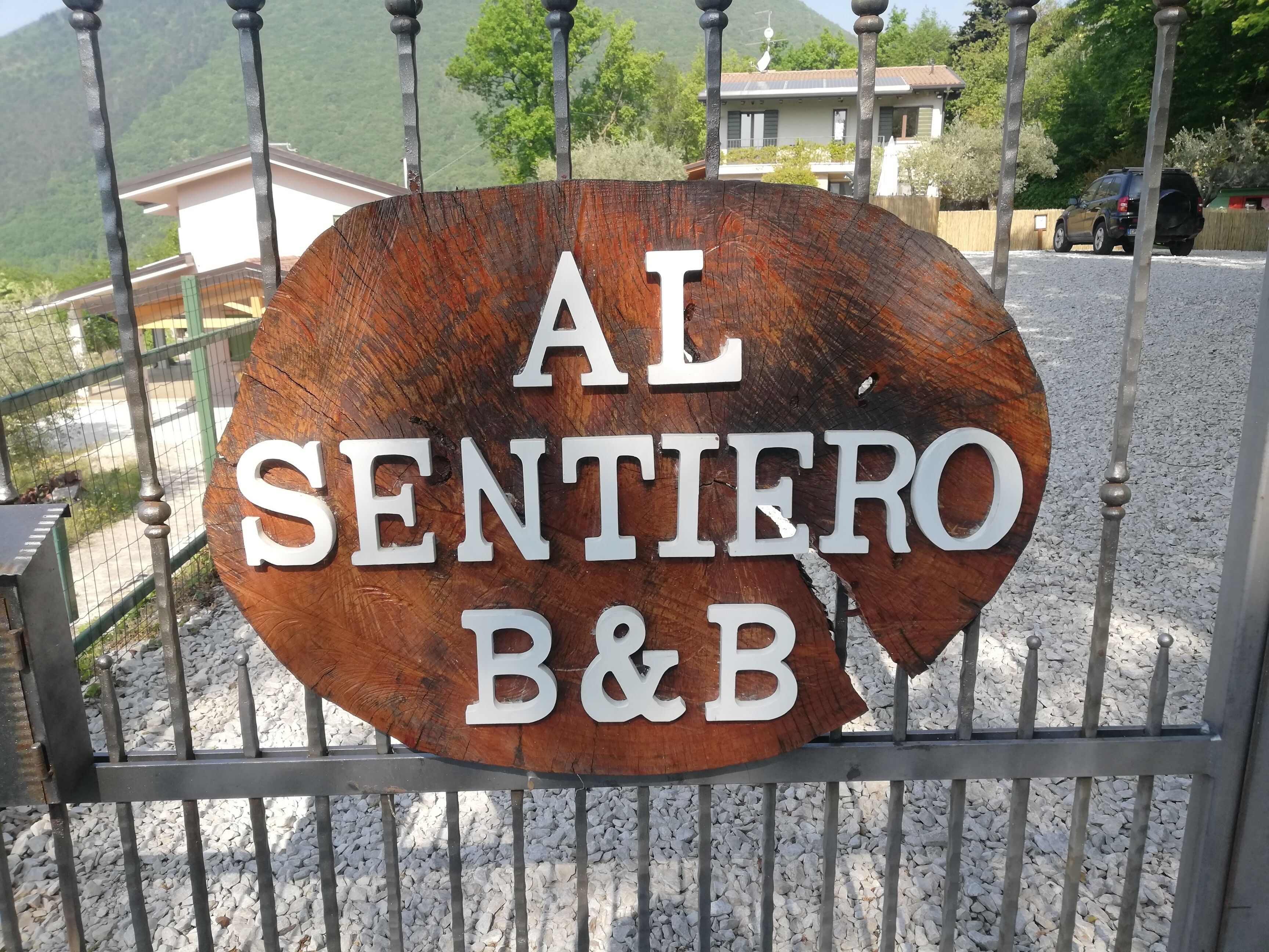 Een houten bord met de tekst 'AL SENTIERO B&B' achter een metalen hek.