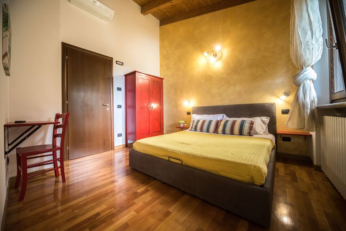 A bedroom with a bed, a red wardrobe, a wooden chair, and a small table.