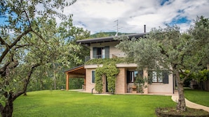 A modern two-story house with a covered patio, surrounded by a well-maintained lawn and olive trees. - B&B Al Sentiero (Caprino Veronese)