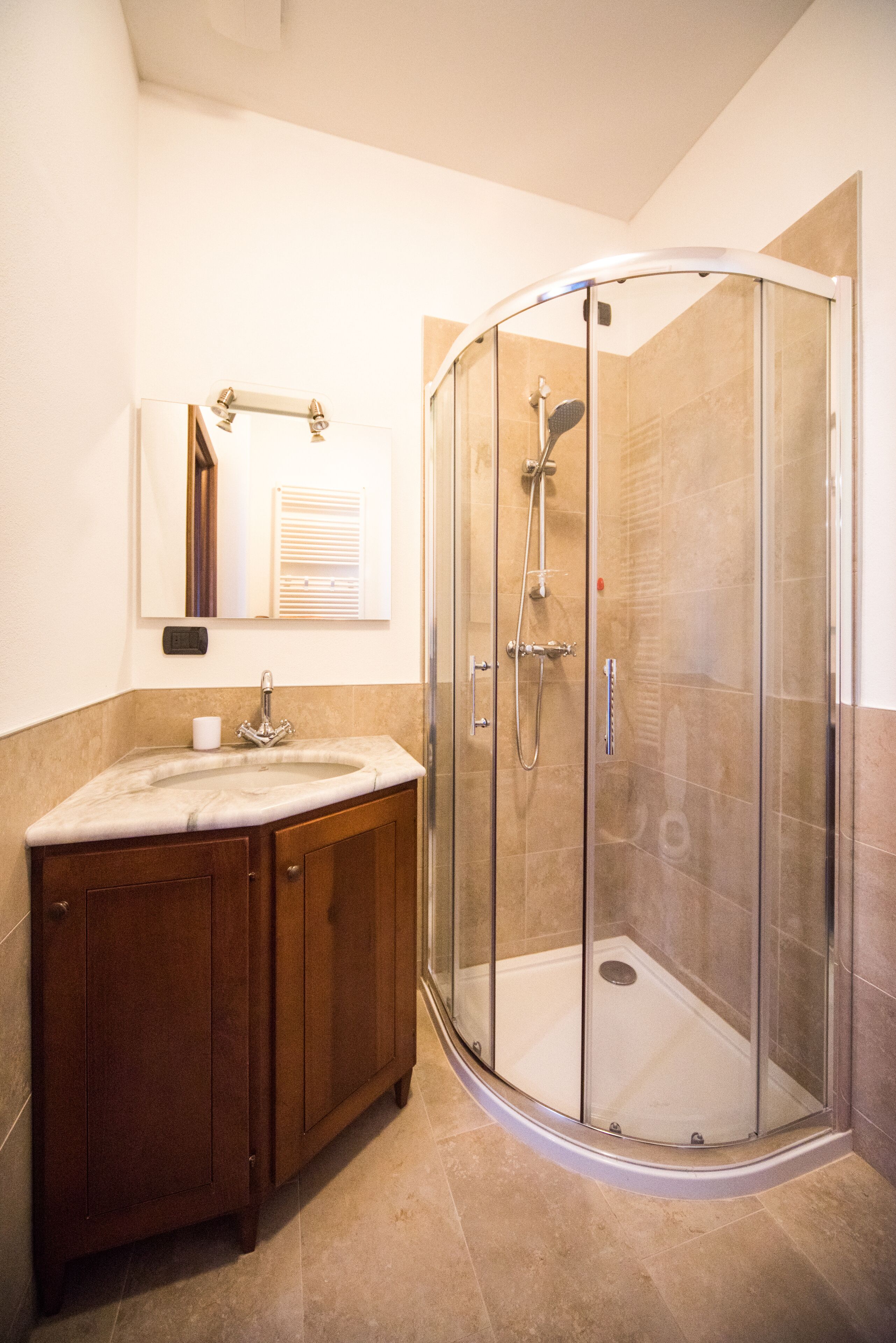 Un baño con ducha envuelta en vidrio, tocador de madera y espejo sobre el lavabo.