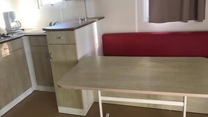 A compact kitchen with a dining table and a red bench. - Camping El Tormes (Alba de Tormes)