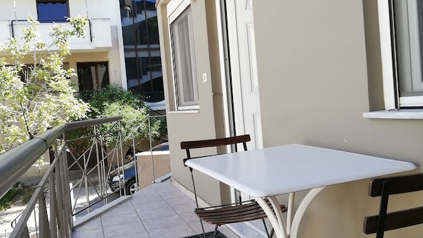 A balcony with a table and chairs, a metal railing, and a view of neighboring buildings.