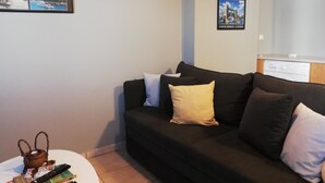 A living room with a black sofa, a white coffee table, and a small table with books and a kettle. There are framed pictures on the wall depicting landmarks.