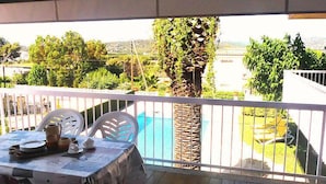 Un balcon avec une table dressée pour les repas, une piscine et une vue sur la verdure et le paysage environnants.