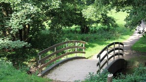 A wooden bridge over a gravel path in a wooded area. - Spangsgaard bed and breakfast (Odense)