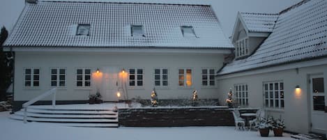A two-story house with a snow-covered roof and steps leading to the front door.