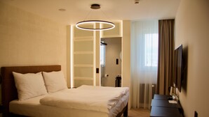 Una habitación de hotel con una cama grande, una mesita de noche, un televisor y un vestidor.