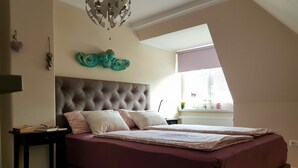 Una camera da letto con una testiera imbottita, un letto con biancheria a fantasia, un comodino con libri e un elemento decorativo a parete.
