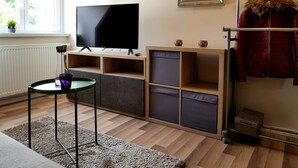 Un soggiorno moderno con una TV a schermo piatto, scaffali in legno, un tavolino e un appendiabiti con una giacca foderata in pelliccia.