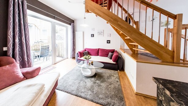 A modern living room with a red sofa, a glass coffee table, and a wooden staircase.